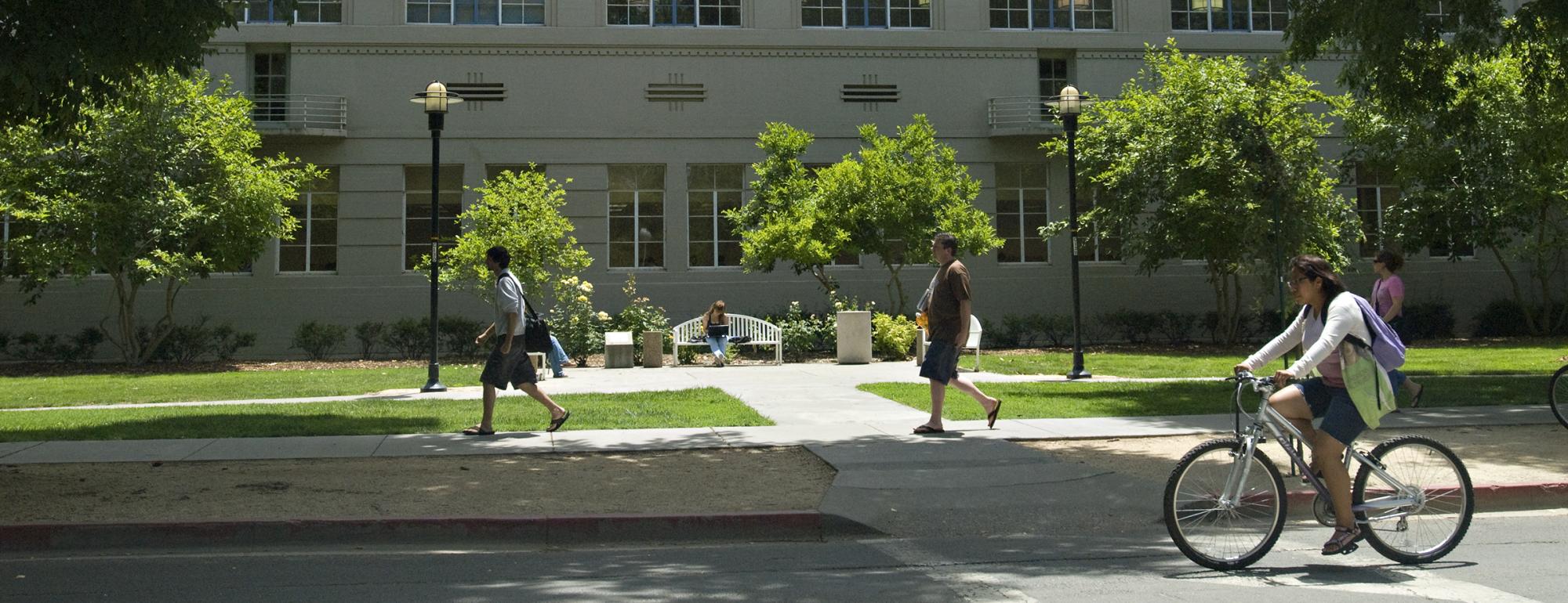 students walking and riding a bike on campus
