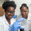 two female students in lab coats look at petri dish